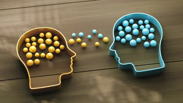 Two cookie cutter style shapes of human heads facing each other, 1 yellow and 1 blue, filled with same colour marbles which are also between them
